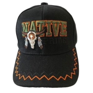 Könnte beinhalten: Schwarze Baseballkappe mit einem orangefarbenen und braunen Stickmuster mit den Worten "NATIVE PRIDE" und einem Totenkopf mit Federn. Der Schirm der Kappe hat ein orangefarbenes Zickzackmuster.