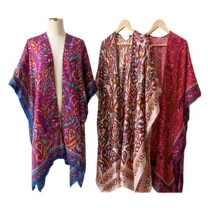 May include: Three patterned kimono-style cover-ups in shades of red, pink, and cream. One is displayed on a mannequin, while the others hang on wooden hangers. The designs feature floral and paisley patterns.