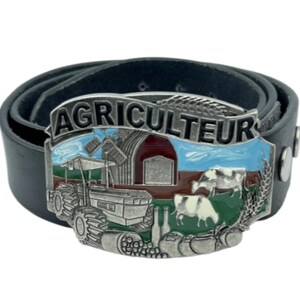 Op de afbeelding: Zwarte leren riem met een zilveren gesp met het woord "AGRICULTEUR" boven een boerderijsc&egrave;ne. De gesp toont een tractor, schuur, koeien en tarwearen, met blauwe, rode en groene accenten.