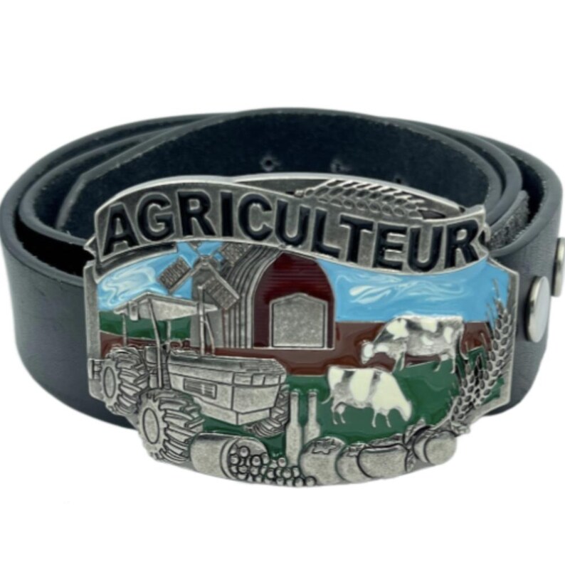 Op de afbeelding: Zwarte leren riem met een zilveren gesp met het woord "AGRICULTEUR" boven een boerderijsc&egrave;ne. De gesp toont een tractor, schuur, koeien en tarwearen, met blauwe, rode en groene accenten.