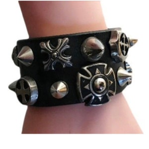 Puede incluir: Un brazalete de cuero negro con tachuelas, púas y abalorios en forma de cruz plateados.