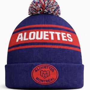 May include: A blue knit beanie with a red band featuring the word "ALOUETTES" in white. The beanie has a red and white pom-pom on top and a circular emblem with the words "ALOUETTES MONTREAL".