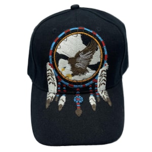 Puede incluir: Gorra de béisbol negra con un diseño de atrapasueños bordado con un águila en el centro. El atrapasueños tiene un borde azul, rojo y amarillo, con plumas blancas colgando debajo. La gorra tiene una visera curva y un botón en la parte superior.