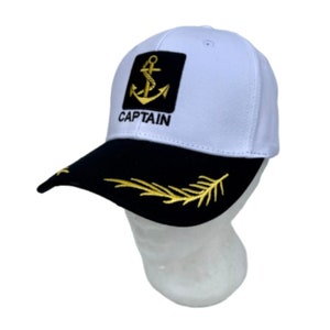 Könnte beinhalten: Weiße Baseballkappe mit schwarzem Schirm und einem goldenen Anker sowie dem Wort "CAPTAIN" bestickt auf der Vorderseite. Der Schirm hat ein goldenes Blattdesign.