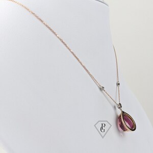 Op de afbeelding: Een delicate ketting van ros&eacute;goud met een hanger van roze edelsteen. De hanger heeft een traanvorm met een gouden frame. De ketting is versierd met kleine diamant accenten.