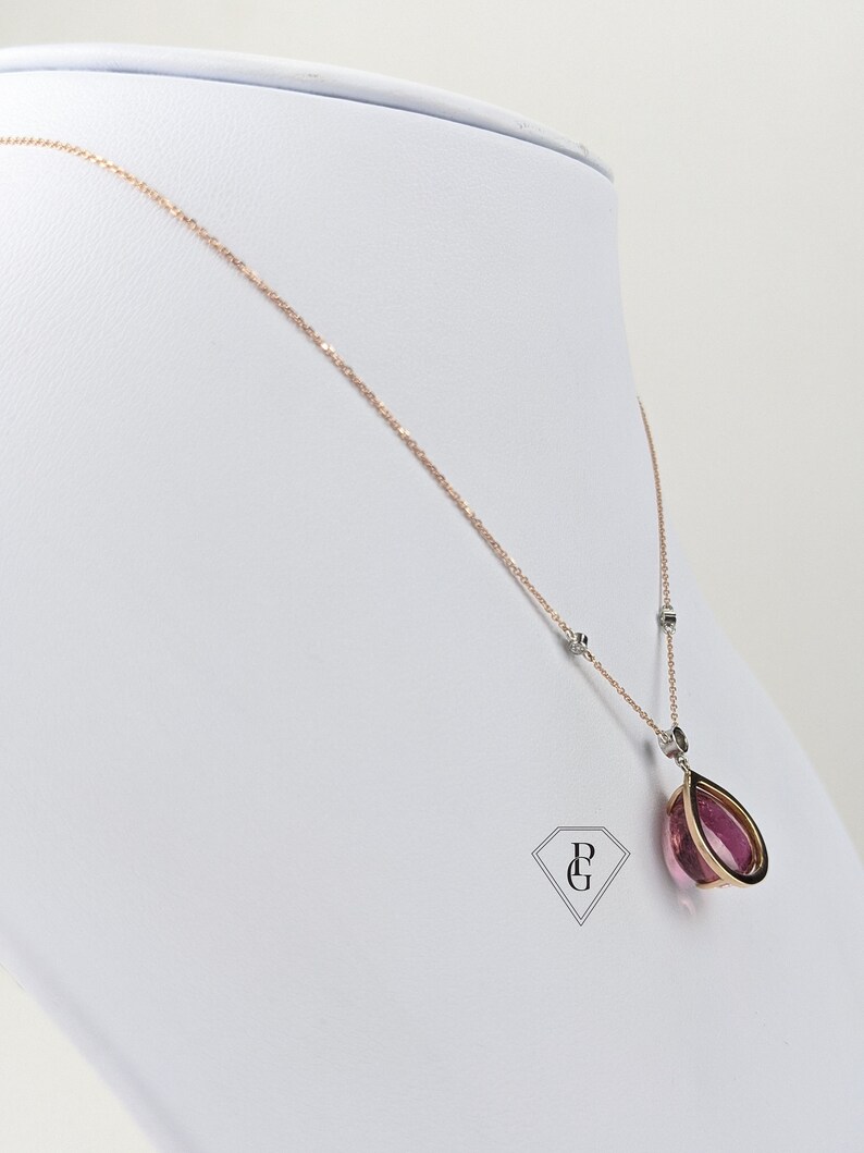 Op de afbeelding: Een delicate ketting van ros&eacute;goud met een hanger van roze edelsteen. De hanger heeft een traanvorm met een gouden frame. De ketting is versierd met kleine diamant accenten.