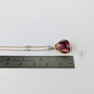 Op de afbeelding: Een ketting van ros&eacute;goud met een hanger van roze edelsteen en twee kleinere diamanten accenten. De ketting wordt gemeten met een liniaal.