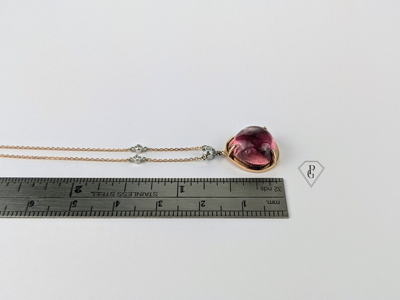 Op de afbeelding: Een ketting van ros&eacute;goud met een hanger van roze edelsteen en twee kleinere diamanten accenten. De ketting wordt gemeten met een liniaal.