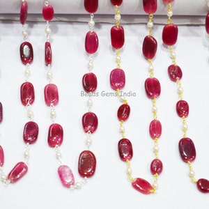 Puede incluir: Cuatro hebras de cuentas de piedras preciosas rojas enhebradas en cadenas de plata y oro con acentos de perlas blancas. Las hebras se muestran sobre una superficie blanca. Beads Gems India está impreso en la superficie.
