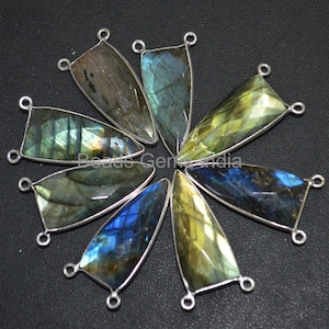 May include: Eight iridescent labradorite gemstone pendants with silver-toned jump rings. The pendants are faceted and have a teardrop shape.