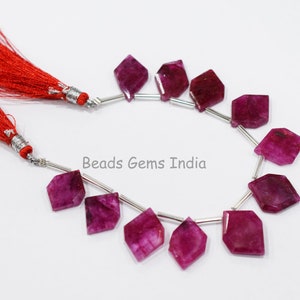 以下が含まれることがあります： 10個のファセットカットされたルビーのビーズのストランド。各ビーズは濃いピンク色で、ダイヤモンドの形をしています。ビーズはシルバーワイヤーに糸に通され、小さなシルバースペーサーで区切られています。ビーズは白い背景に表示されています。