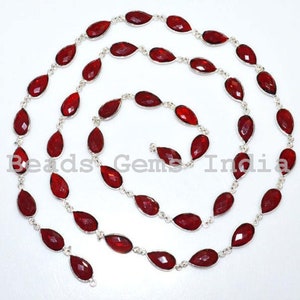 Puede incluir: Una larga hebra de cuentas de piedras preciosas rojas conectadas por eslabones de cadena plateados. Las cuentas son facetadas y tienen forma de lágrima.