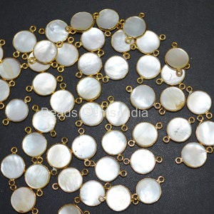 Puede incluir: Un grupo de cuentas redondas de madreperla blanca con detalles metálicos dorados. Cada cuenta tiene tres bucles para sujetar a la joyería.