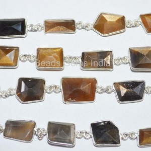 May include: A strand of gold and black sunstone beads connected by silver chain links. The beads are faceted and have a rectangular shape.