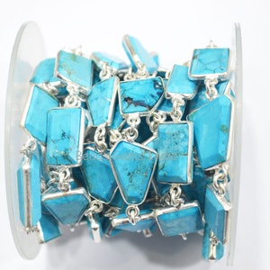 May include: A turquoise gemstone chain with silver accents. The chain is made of rectangular turquoise stones with silver frames and silver connectors. The chain is wound around a spool.