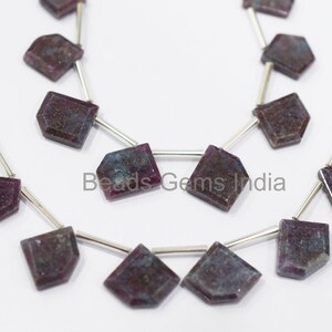 May include: A strand of faceted gemstone beads in shades of purple and blue. The beads are strung on silver wire and have a faceted, irregular shape. The beads are approximately 10mm in size. Beads Gems India is printed on the white background.