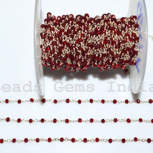 May include: A spool of red glass bead chain with silver chain links. The chain is wound around a clear plastic spool. The chain is shown in three straight lines on a white background.