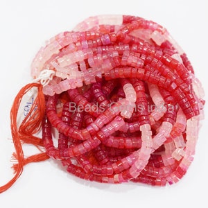 May include: A strand of pink and red gemstone beads. The beads are square and have a slightly rounded edge. The beads are strung on a thin string.