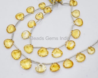 May include: A strand of yellow gemstone beads, each bead is a faceted heart shape, strung on silver wire. The beads are arranged in a double strand, with the beads on the top strand slightly larger than the beads on the bottom strand. The beads are all approximately the same size and shape. The strand is approximately 18 inches long. Beads Gems India is printed on a white background.