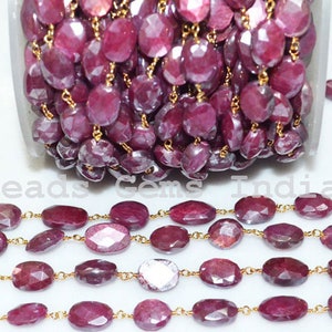 May include: A strand of ruby gemstone beads with gold chain links. The beads are faceted and have a deep red color. The chain is made of gold-plated metal. Beads Gems India is printed on the background.