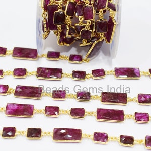 Könnte beinhalten: Eine goldene Kette mit rechteckigen, violetten Edelsteinperlen. Die Kette liegt in Reihen auf einer weißen Oberfläche.