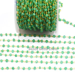 Könnte beinhalten: Eine grüne Edelsteinkette mit goldenen Akzenten. Die Kette besteht aus kleinen, facettierten grünen Edelsteinen und goldenen Kettengliedern. Die Kette liegt in einer geraden Linie auf einem weißen Hintergrund.