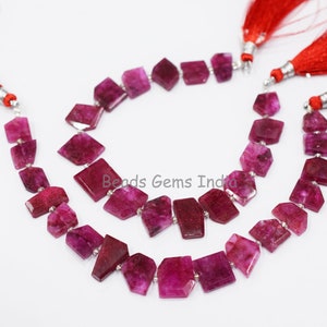 May include: Two strands of pink gemstone beads with faceted square shapes. The beads are strung on silver wire and have red tassels on each end.