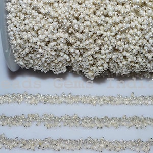 May include: A silver and white bead chain, wound around a spool. The chain is made of small, round beads, some silver and some white.