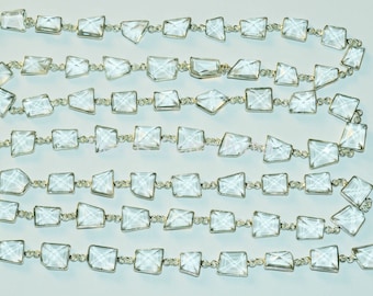 Può includere: Una fila di perline di cristallo trasparente infilate su una catena d'argento. Le perline sono sfaccettate e hanno una forma quadrata.
