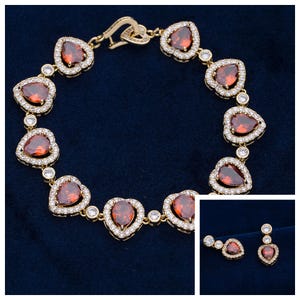 Peut inclure: Ensemble de bracelet et boucles d'oreilles dorés. Le bracelet présente des pierres précieuses rouges en forme de cœur entourées de petites pierres claires. Les boucles d'oreilles ont une pierre en forme de cœur assortie et une petite pierre ronde.