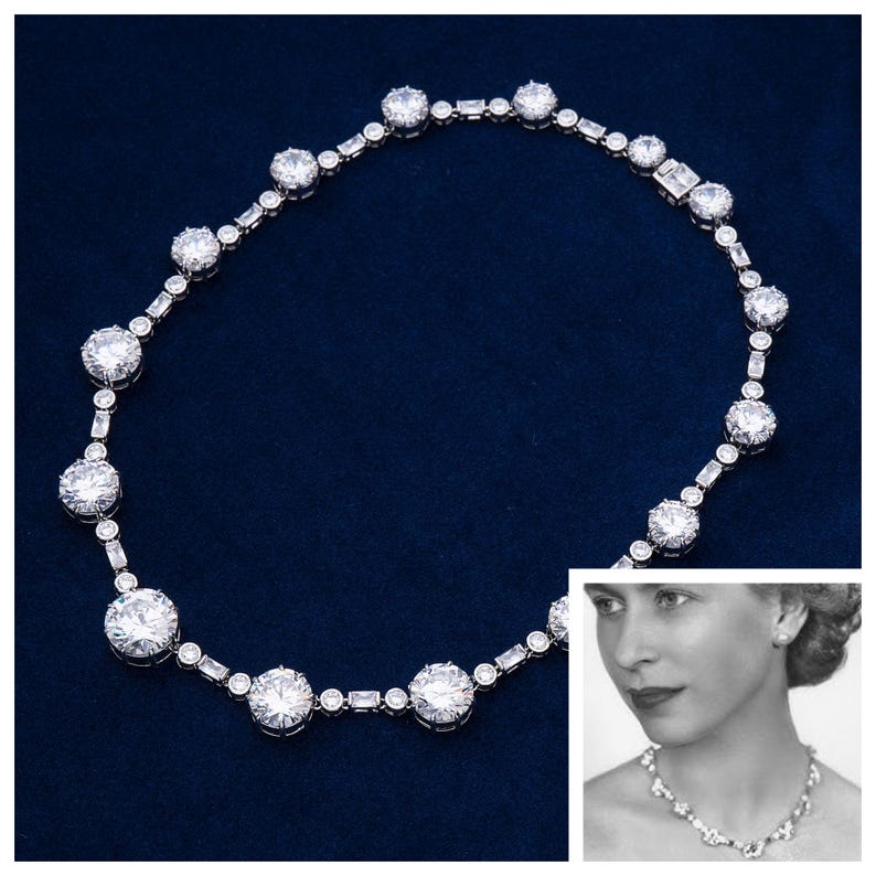 May include: A sparkling necklace with large, round, and rectangular-cut clear gemstones set in a silver-toned metal. The necklace is displayed on a dark blue background. A black and white photo of a person wearing a similar necklace is in the corner.