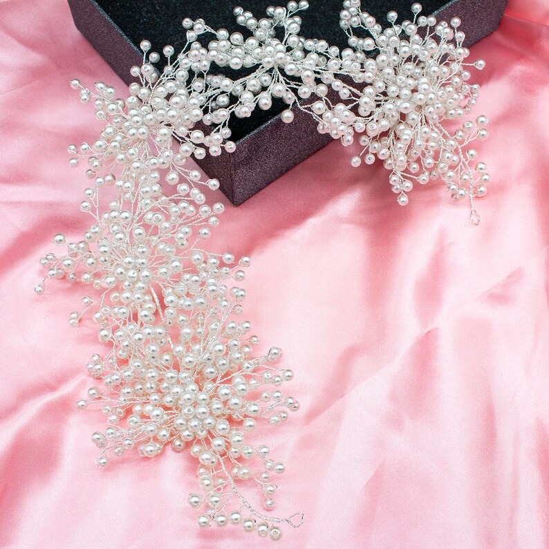 May include: A long, white pearl hair vine with a delicate, floral design. The vine is made of small, white pearls strung on a silver wire. The vine is perfect for adding a touch of elegance to any hairstyle.