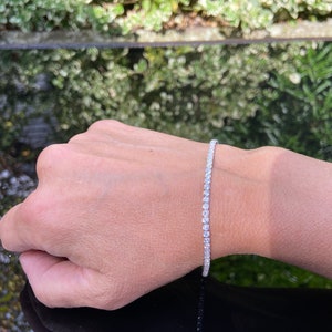 Puede incluir: Un brazalete de tenis plateado con pequeñas piedras redondas transparentes.