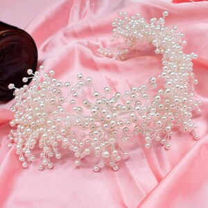 May include: A white pearl headband with a delicate, floral design. The headband is made of small, white pearls strung on thin wire.