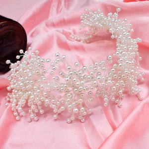 May include: A white pearl headband with a delicate, floral design. The headband is made of small, white pearls strung on thin wire.
