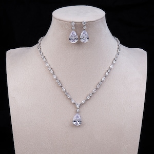 Può includere: Una collana d'argento con un ciondolo a forma di pera e orecchini abbinati. La collana e gli orecchini sono adornati con pietre di zircone cubico trasparenti.