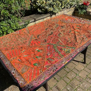 May include: A large, colourful tapestry with intricate embroidery and beading. The tapestry is made up of various patchwork pieces in shades of orange, red, pink, and green. It features a floral design and is accented with gold and silver thread.