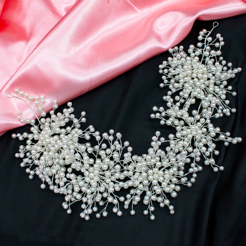 May include: A delicate pearl hairpiece with a floral design. The hairpiece is made of silver wire and white pearls. It is perfect for a wedding or special occasion.