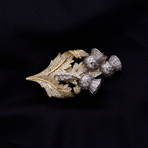 May include: A gold and silver brooch with a thistle design. The brooch is adorned with sparkling clear rhinestones.