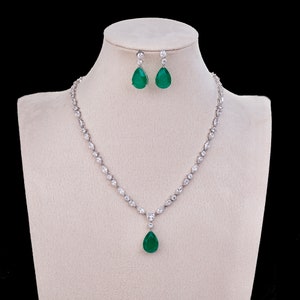 May include: A silver necklace with a teardrop-shaped green stone pendant and matching earrings. The necklace is made of small, clear stones.