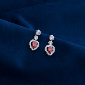 Peut inclure: Une paire de boucles d'oreilles en argent avec des pierres en forme de cœur rouges et des accents de zircone cubique clairs.