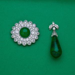 May include: A floral-shaped brooch and a teardrop pendant, both featuring a vibrant green center stone surrounded by sparkling clear crystals. The jewelry is set against a solid green background.