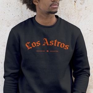 May include: Black sweatshirt with an orange graphic that says "Los Astros" in a stylized font. The graphic also includes the text "Hecho en Houston" with a small outline of the state of Texas.