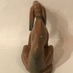 May include: A brown ceramic figurine of a dog sitting with its head down. The dog has long ears and a short tail.
