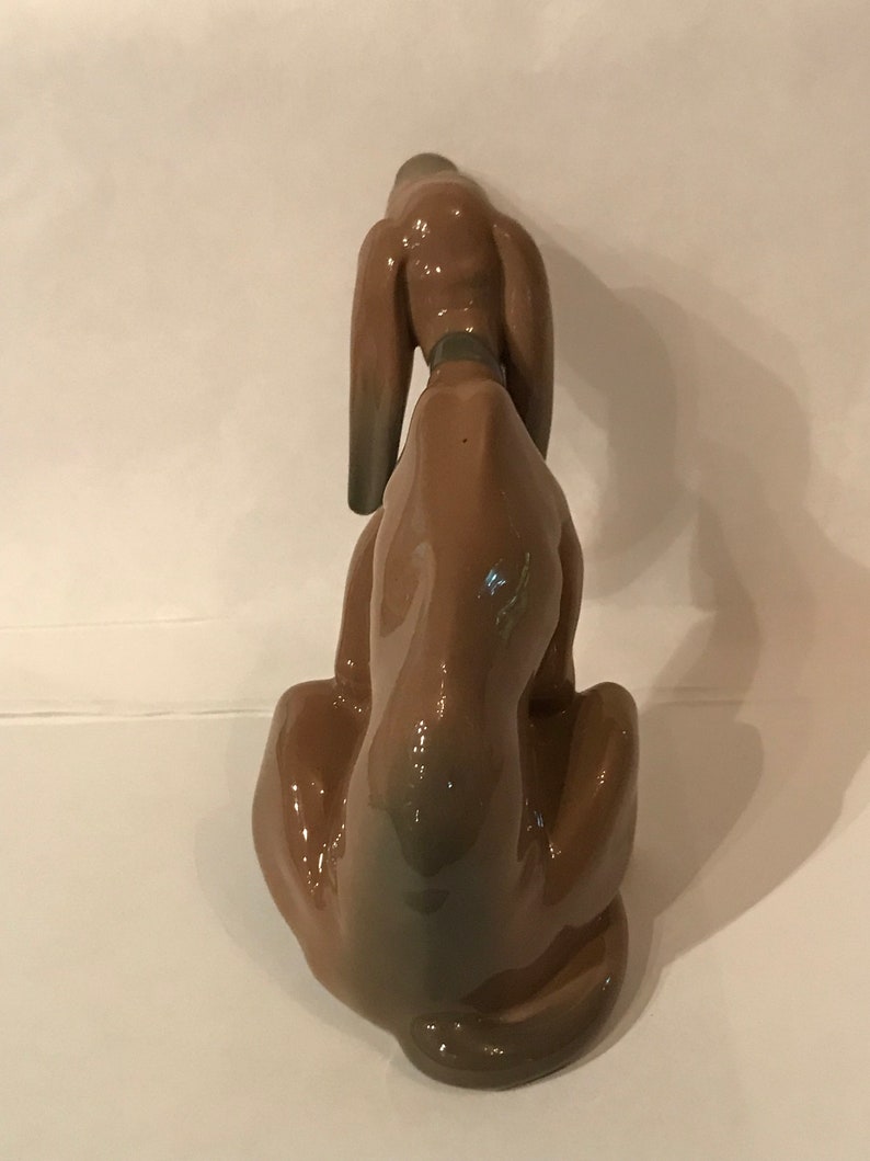 May include: A brown ceramic figurine of a dog sitting with its head down. The dog has long ears and a short tail.