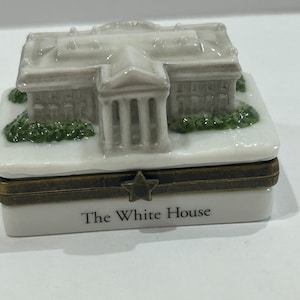 May include: A white porcelain trinket box with a miniature replica of the White House on the lid. The box has a gold star and the words "The White House" on the front.