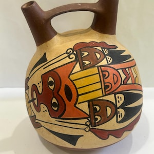 May include: A brown ceramic pitcher with two spouts and a handle. The pitcher is decorated with a geometric design in red, orange, yellow, and black.