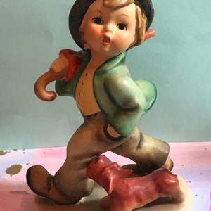 May include: A figurine of a boy wearing a green jacket, black hat, and brown pants, holding an umbrella and walking with a brown dog.