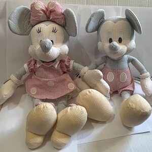 Puede incluir: Dos mu&ntilde;ecos de peluche de Mickey y Minnie Mouse. Mickey lleva pantalones cortos rojos, y Minnie lleva un vestido y un lazo a rayas rojas y blancas. Ambos mu&ntilde;ecos tienen cuerpos a rayas azules y blancas y manos y pies color crema.