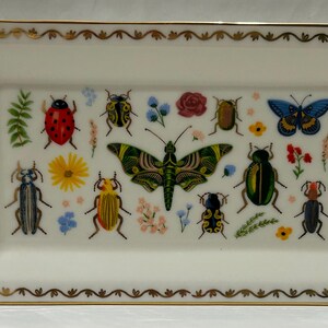 May include: A white rectangular ceramic tray with a gold rim and a decorative design of colorful insects and butterflies. The tray features a variety of insects, including ladybugs, beetles, and butterflies, all with intricate details.